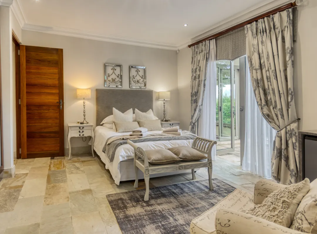 The elegant Le Jardine bedroom at Bonne Chance estate, showcasing a bed, chair, table, and a sliding glass door.