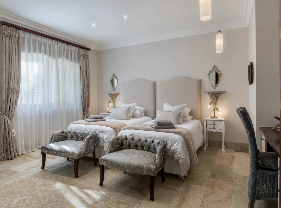 The L'Olivier room at Bonne Chance estate showcases a stylish bedroom with two beds and a comfortable chair.